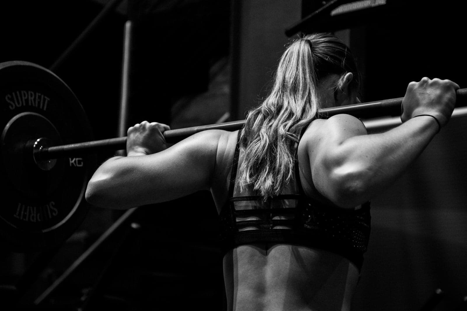Athletic woman with a barbell across her shoulders in a dark gym