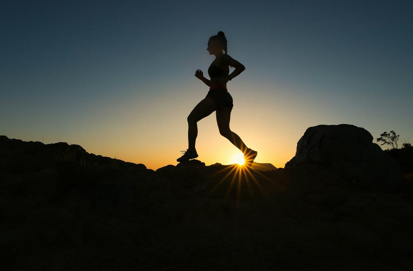 Silhouette of a woman running across rocks at sunset