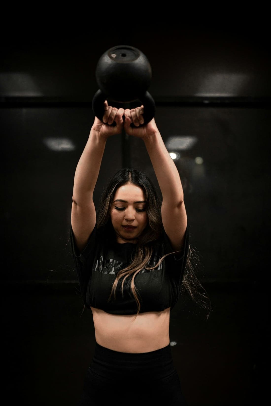 Woman pressing a kettlebell overhead in a dark gym